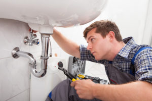 young man providing plumbing services to a pipe under a sink