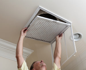 Senior male reaching up to open filter holder for air conditioning filter in ceiling probably connected to his swamp cooler