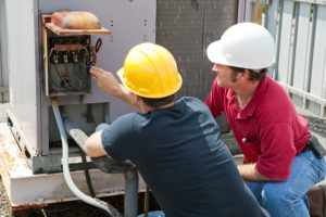 Two technicians repairing an icommercial HVAC's compressor