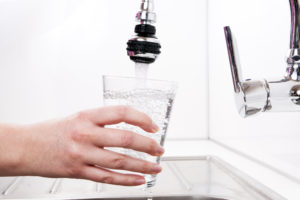 hand holding a glass underneath a tap that may be filtered through home water filters
