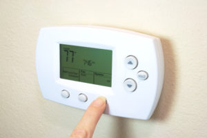 close up of hand clicking thermostat for heating and cooling system